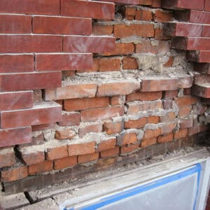 Historic brick wall with extensive brick deterioration, missing bricks, and failed mortar joints requiring structural brick repair.
