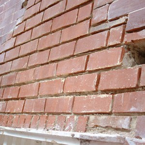 Close-up of a red brick wall with areas of spalled brick, missing brick faces, and deteriorated mortar joints.
