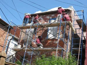 Masonry restoration crew performing tuckpointing on a multi-story historic brick building from scaffolding in Washington, DC.