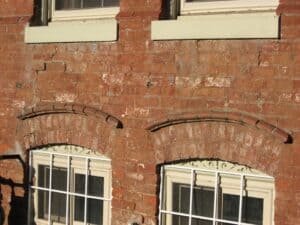 Historic brick façade with lime-mortar joints surrounding arched window openings.