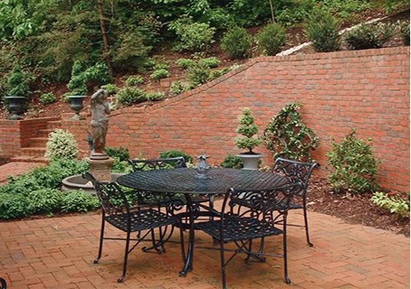 A backyard patio setting with iron table and chairs on a brick patio with brick retaining wall in the background.