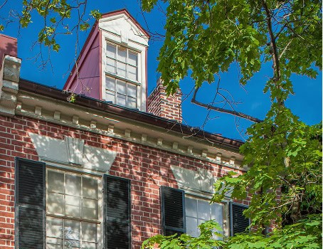 A historic brick building, nicely shaded by the surrounding trees.