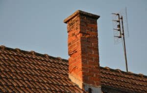 Historic brick chimney showing deteriorated mortar joints and damaged masonry on the roof of an older brick building.