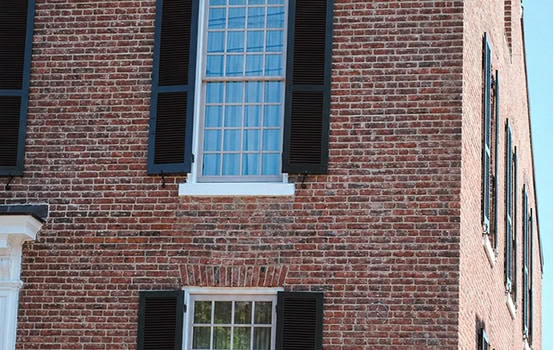 Close-up of historic brick masonry with black shutters on a building facade.