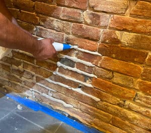 Skilled worker applying mortar to historic brick wall for tuckpointing restoration.
