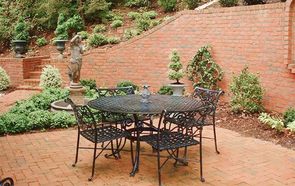 Brick patio with wrought iron table and chairs in a landscaped garden setting.