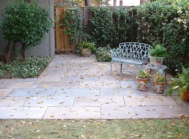 Beautiful backyard patio with stone paving, lush greenery, and vintage garden furniture.