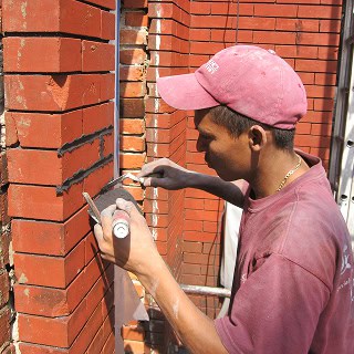 Worker applying tuckpointing on historic brick wall.
