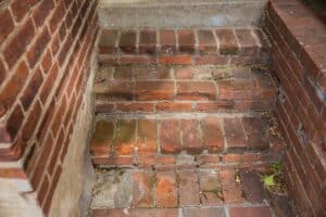 Historic brick steps with deteriorated mortar joints, loose bricks, and vegetation growing between the masonry.