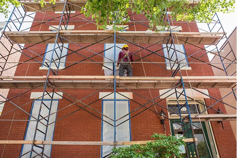 Skilled worker restoring historic brick masonry on a Renaissance building with scaffolding.