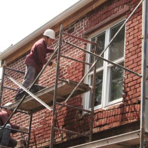 Masonry worker repairing brickwork on historic building with scaffolding.