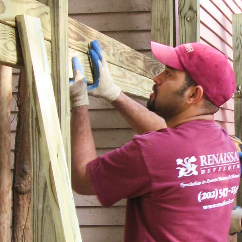 Masonry worker in maroon shirt and cap installing brickwork on a wooden structure.