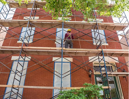 Worker on scaffolding restoring brick masonry and tuckpointing.