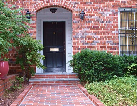 Brick entrance with black door and surrounding greenery, historic masonry work.
