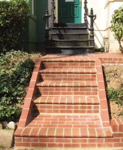 Historic brick stairs with black wrought iron railing at a residential entrance.