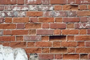 A historic brick wall with white efflorescence, deteriorated mortar joints, and displaced bricks shows advanced masonry deterioration.