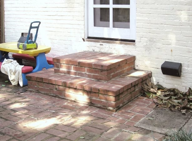 Brick steps leading to a white house with a window, showcasing historic masonry work.