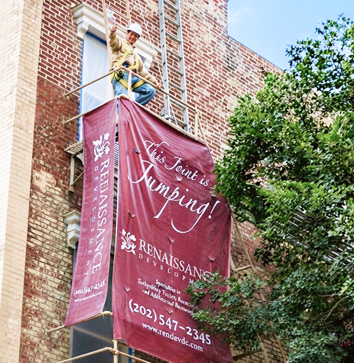 Worker installing Renaissance development banner on brick building